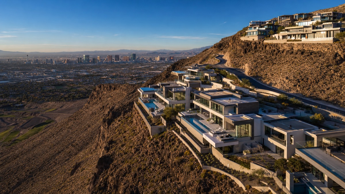 Aerial view of guard-gated luxury communities in Henderson including MacDonald Highlands, Ascaya, and Dragon Rock stepped into the McCullough Range hillside with private estates and resort pools visible across the master-plan footprint